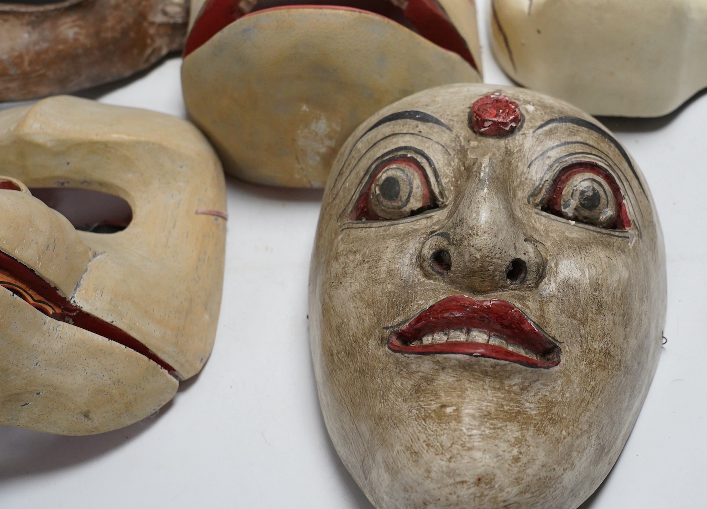 Two pottery face masks, and three pairs of carved and painted masks, largest mask 21cm high